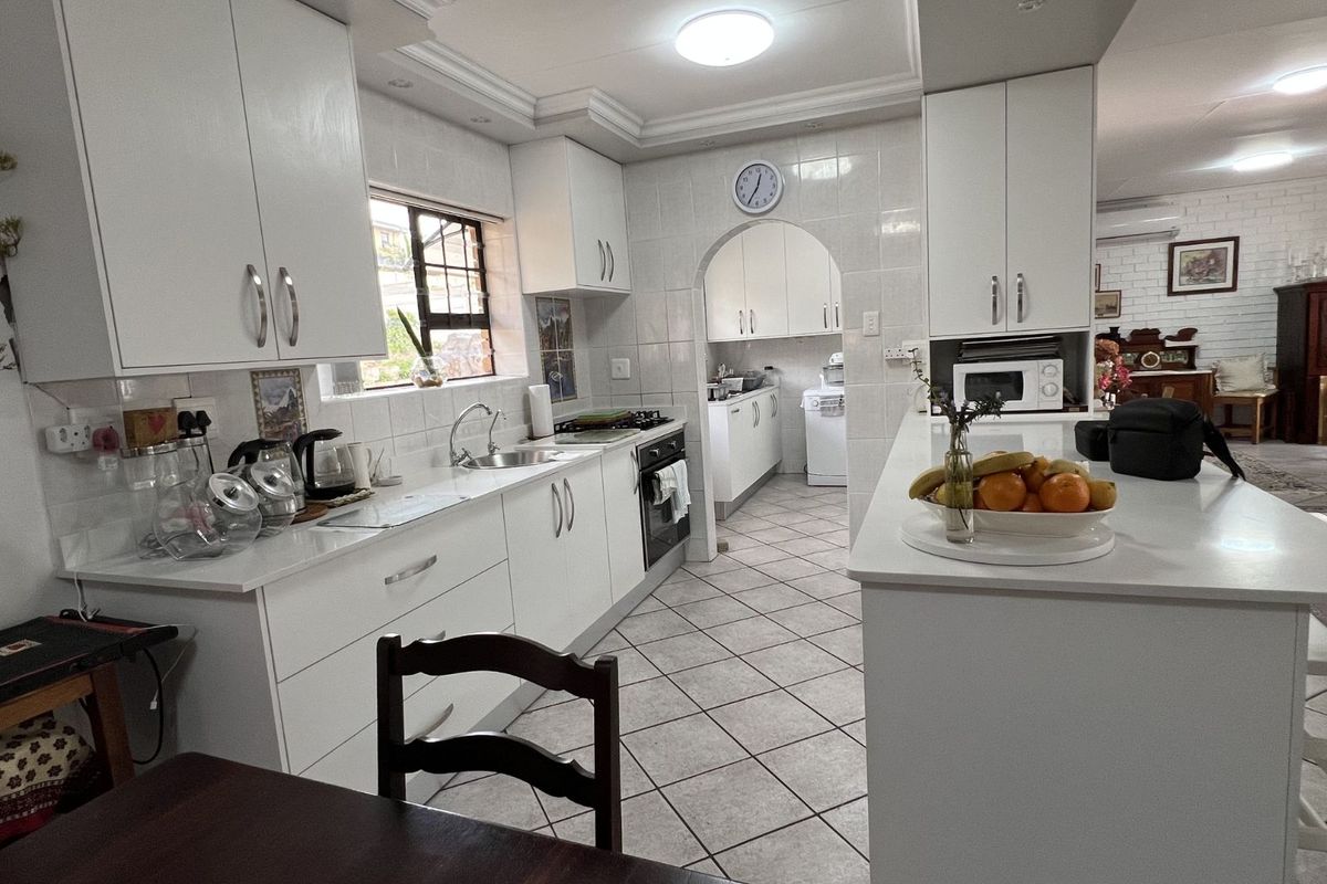 A functional kitchen featuring white cabinetry, tiled splashbacks, a central island, and an adjoining scullery area with tiled flooring throughout.