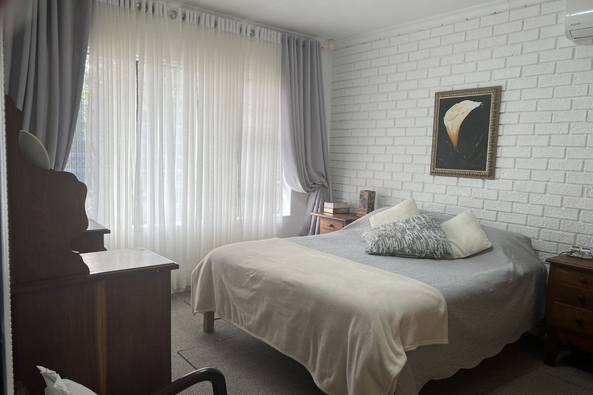 A bedroom featuring a white painted brick feature wall, carpeted flooring, and a wall-mounted air conditioning unit.