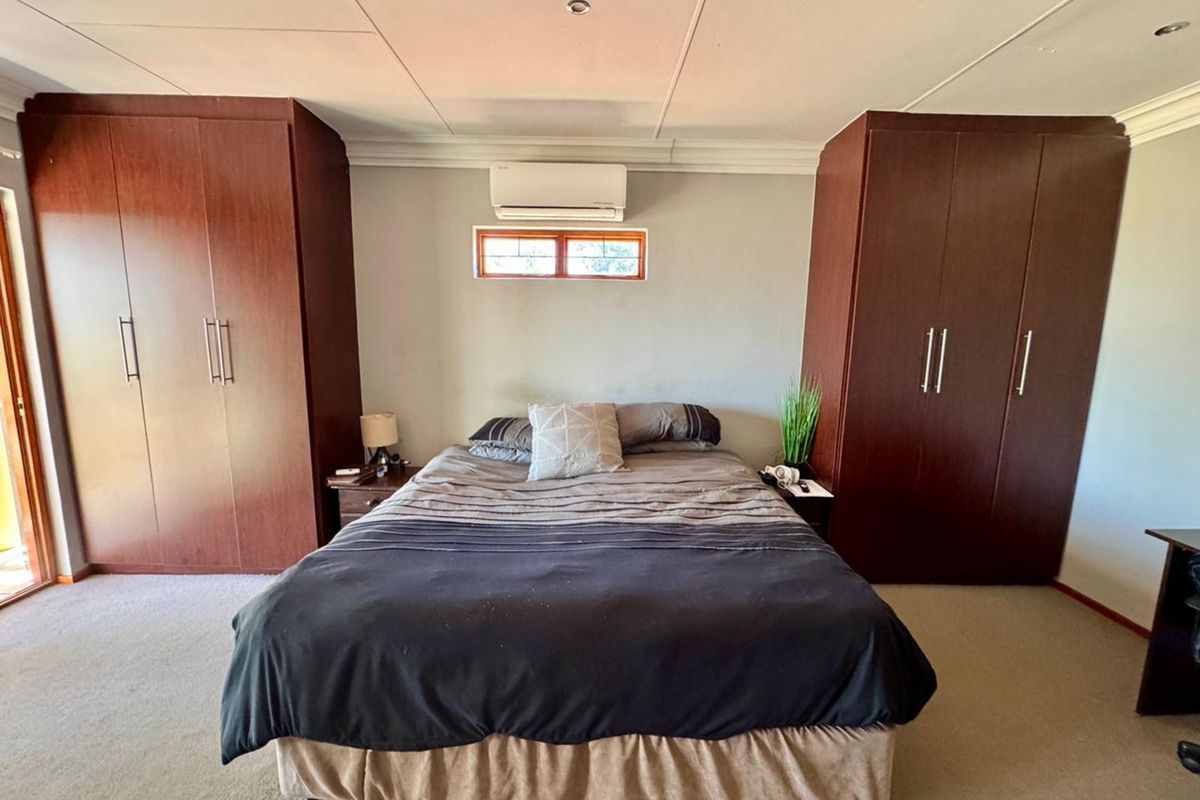 A bedroom featuring built-in dark wood wardrobes, a wall-mounted air conditioning unit, and neutral carpeting.