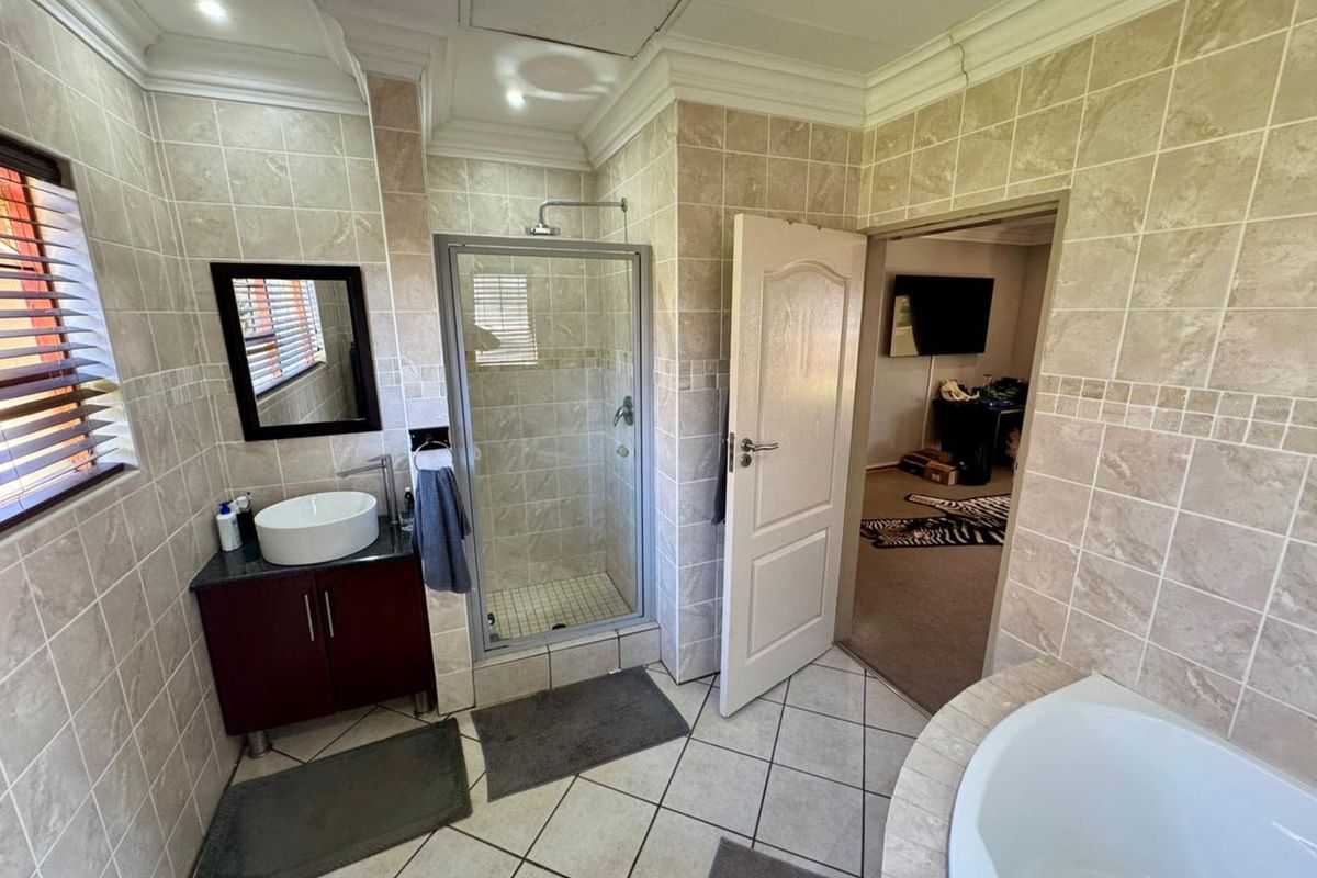 A functional bathroom featuring a glass-enclosed shower, a built-in vanity with a vessel sink, and a corner bathtub with neutral wall tiling.