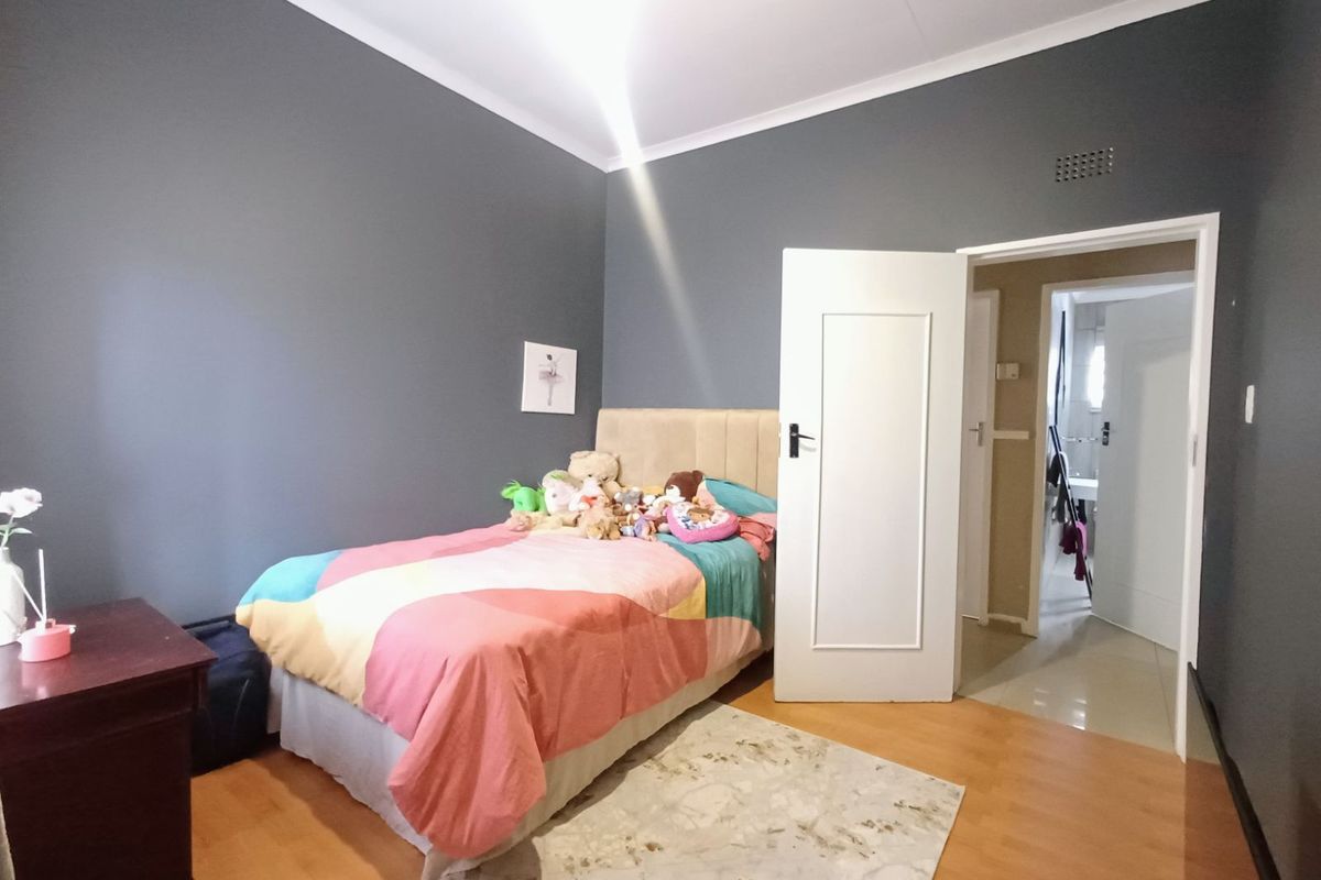 A bedroom featuring laminate flooring, dark grey painted walls, and a white door leading to an adjacent hallway.