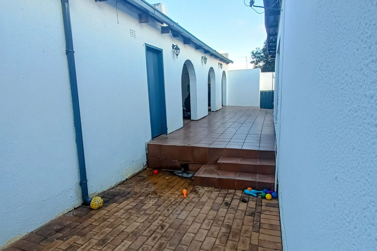 A side exterior walkway featuring tiled steps leading to an arched patio area with brick paving and white rendered walls.