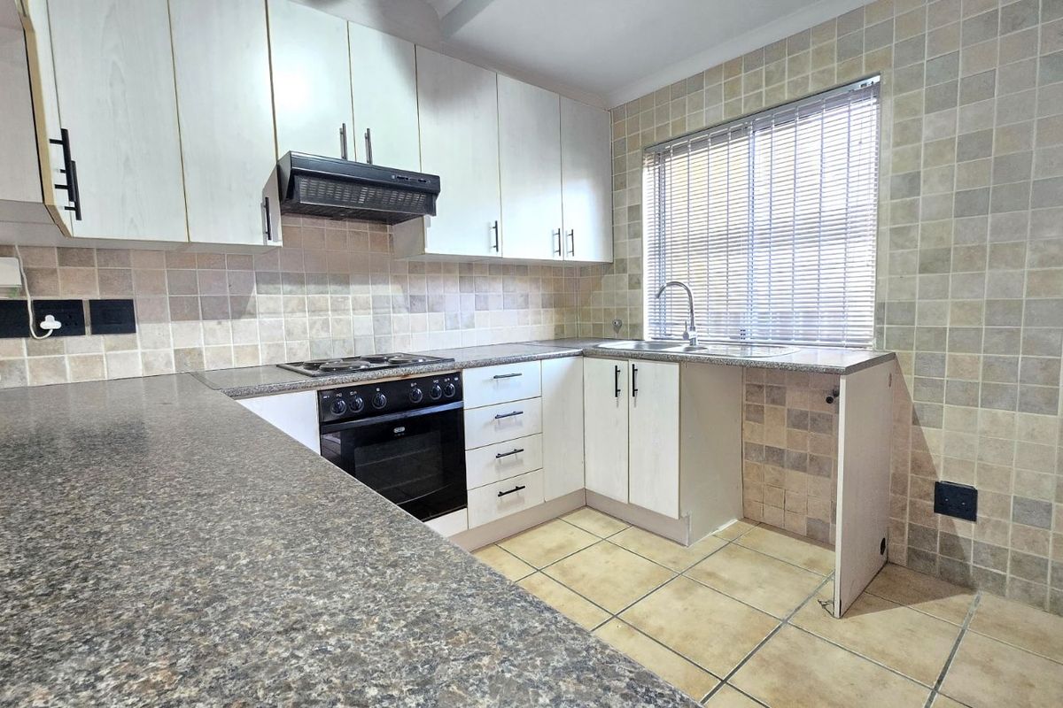 A functional kitchen featuring light-toned cabinetry, granite-look countertops, a built-in oven with extractor fan, and tiled splashbacks.