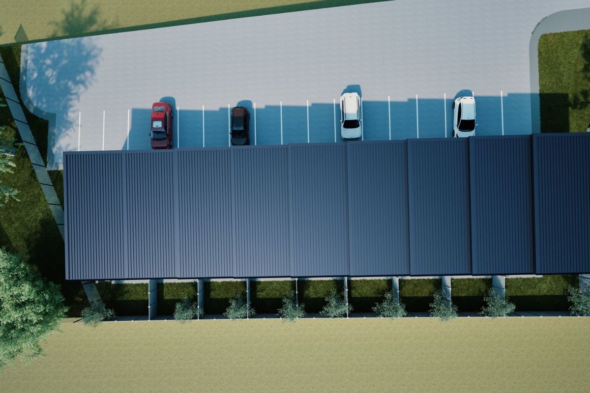 An aerial view of a modern building with a corrugated metal roof, featuring a paved parking area with marked bays.