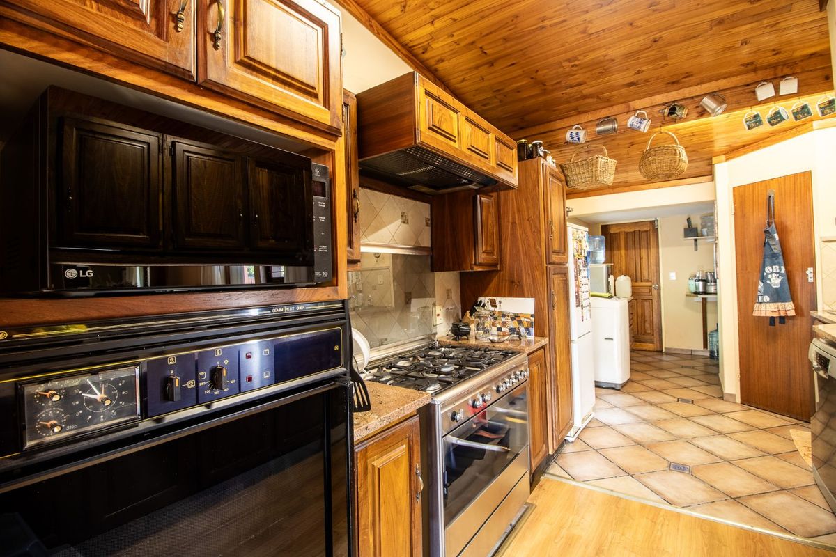 A traditional kitchen featuring wood cabinetry, a built-in oven, gas hob, and tiled flooring, leading into a secondary utility or scullery area.