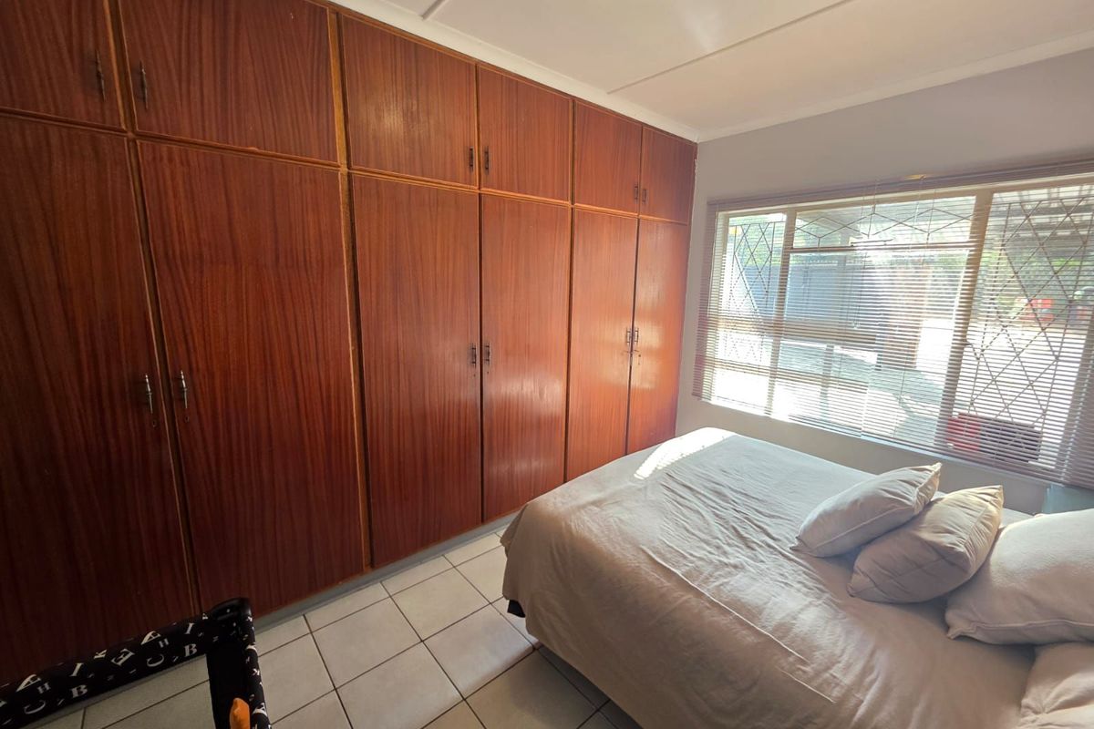 A bedroom featuring extensive floor-to-ceiling built-in wooden cabinetry, tiled flooring, and a large window with security bars.
