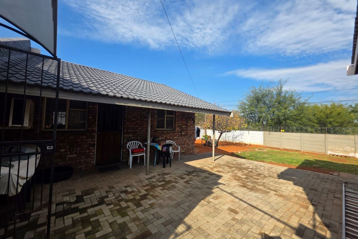 A rear exterior view of the house featuring a covered patio area with paved flooring and a private garden with perimeter walling.