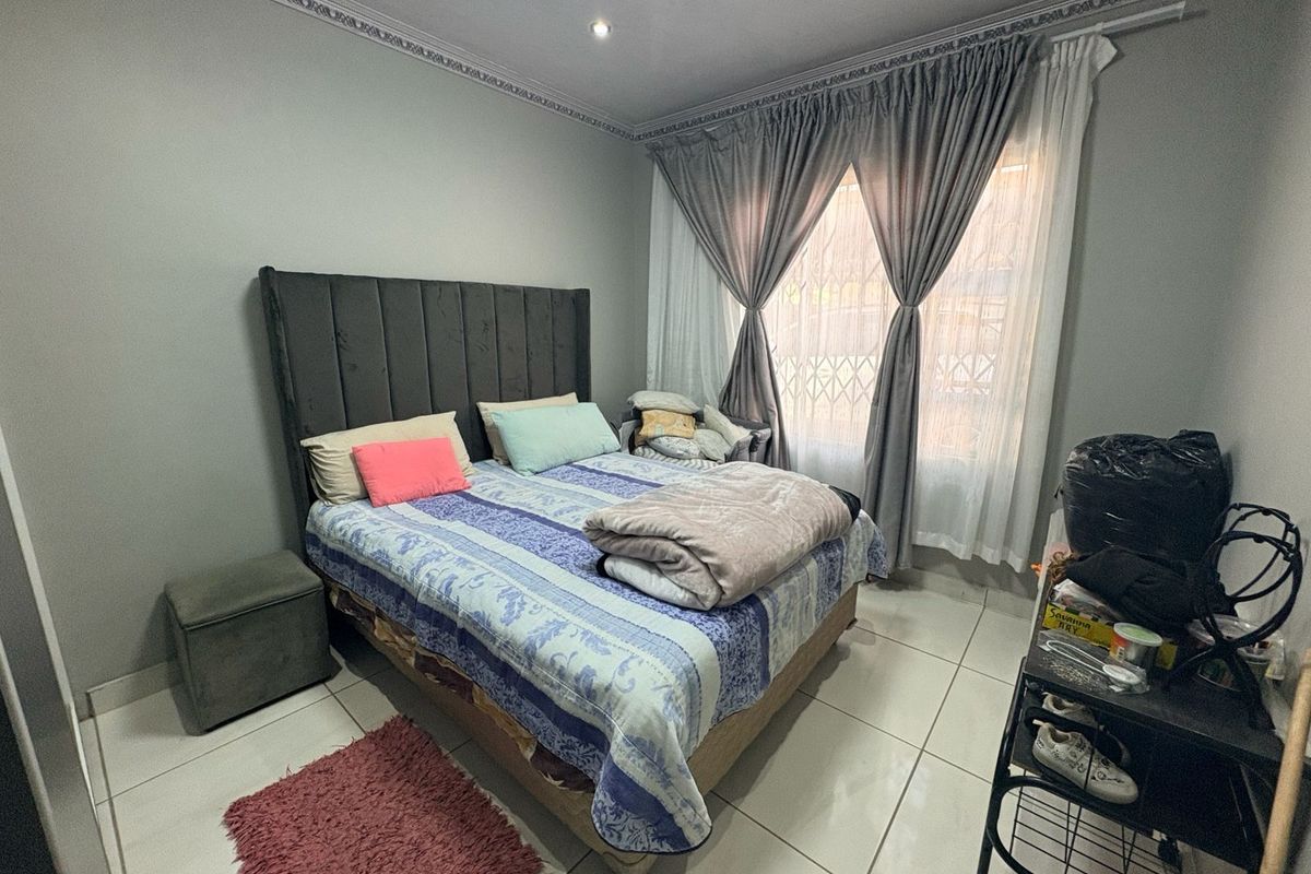 A bedroom featuring tiled flooring, decorative crown molding, and a window with fitted curtains and security gate.