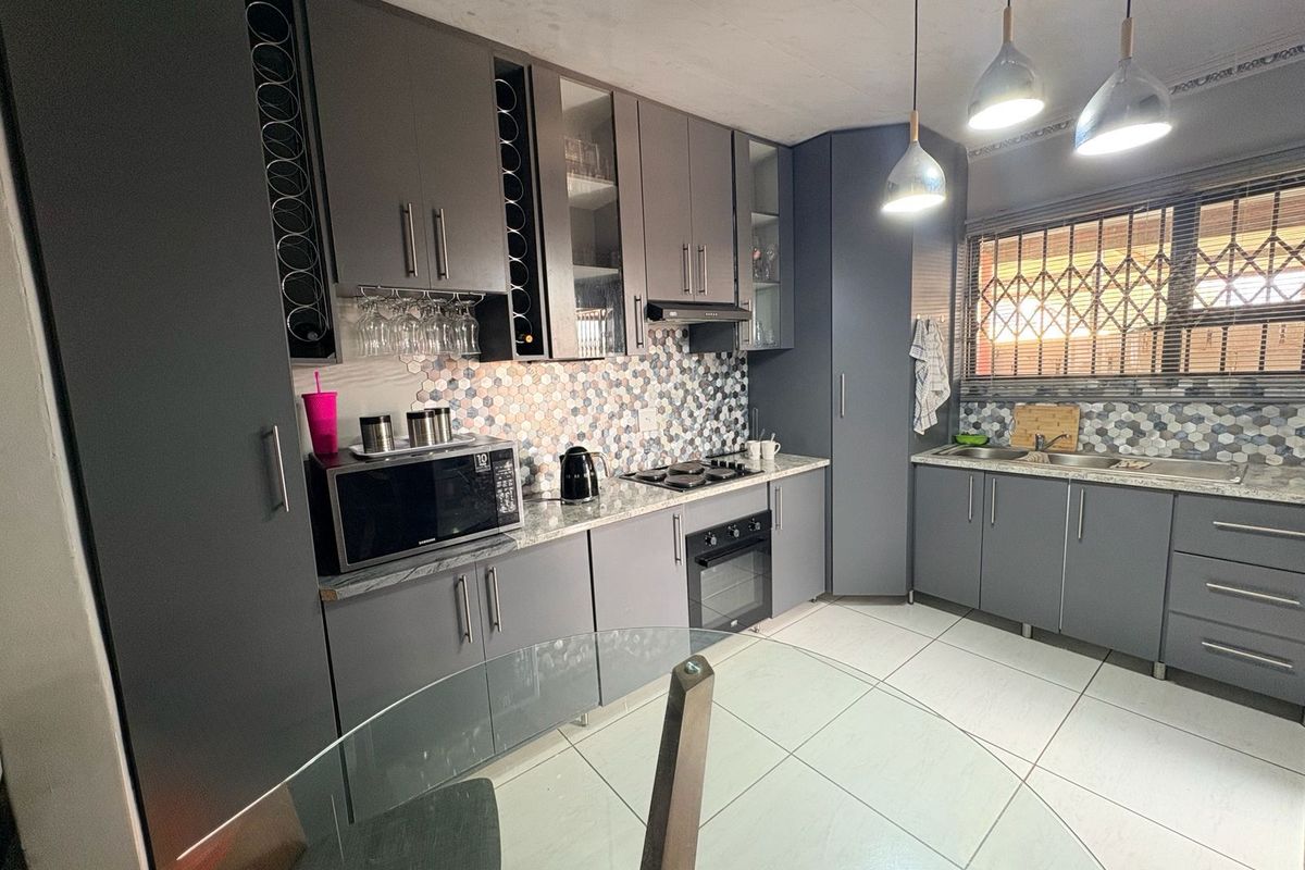 Modern kitchen featuring dark grey cabinetry, granite countertops, a hexagonal mosaic tile backsplash, built-in oven, hob, extractor fan, and double stainless steel sink.