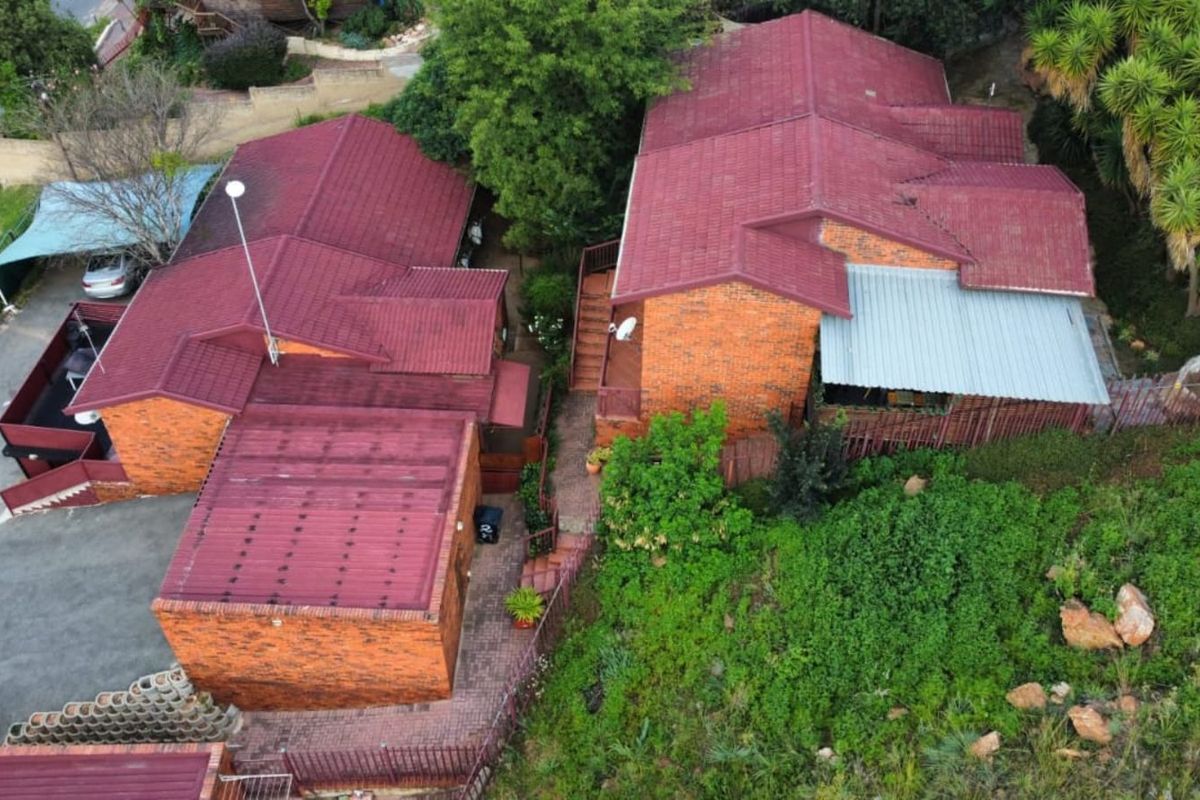 Aerial view of a brick townhouse complex featuring multiple pitched roofs, paved driveway areas, and established surrounding garden landscaping.