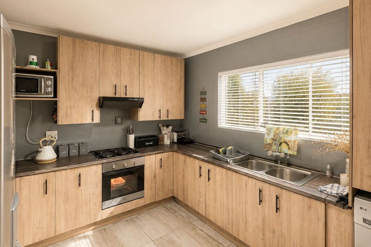Modern kitchen featuring light wood-grain cabinetry, dark laminate countertops, a built-in oven, hob, extractor fan, and a double stainless steel sink.