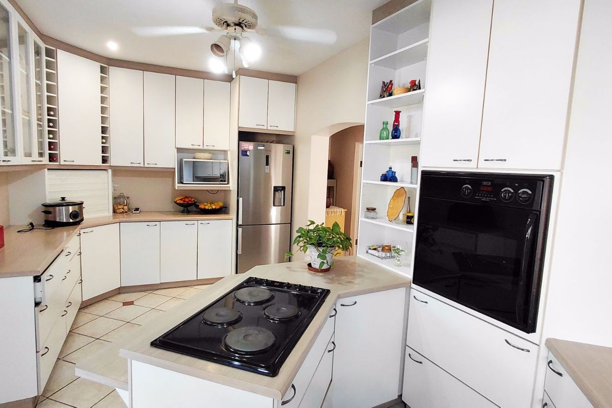 A well-appointed kitchen featuring white cabinetry, a central island with a built-in electric hob, and integrated wall-mounted oven.