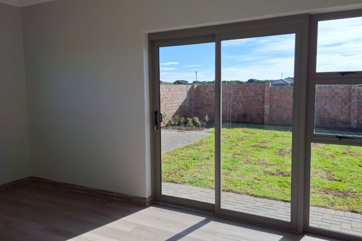 A bright, empty living room featuring modern laminate flooring and large sliding glass doors that open onto a private rear garden.