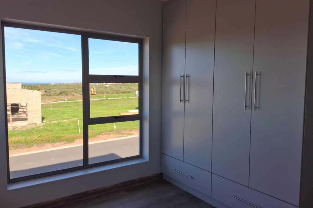 A bright bedroom featuring modern built-in cupboards and large windows with views of the surrounding landscape.