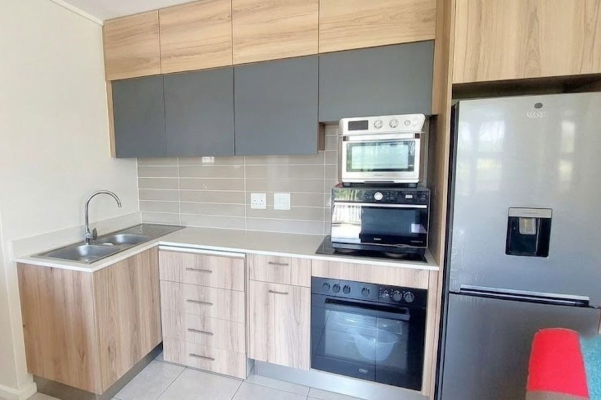 Modern kitchen featuring wood-grain and grey cabinetry, tiled backsplash, built-in oven, hob, and integrated space for a large refrigerator.
