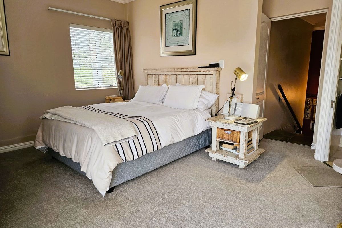 A comfortable bedroom featuring neutral wall tones, carpeted flooring, and a window with fitted blinds, providing a functional and inviting sleeping space.