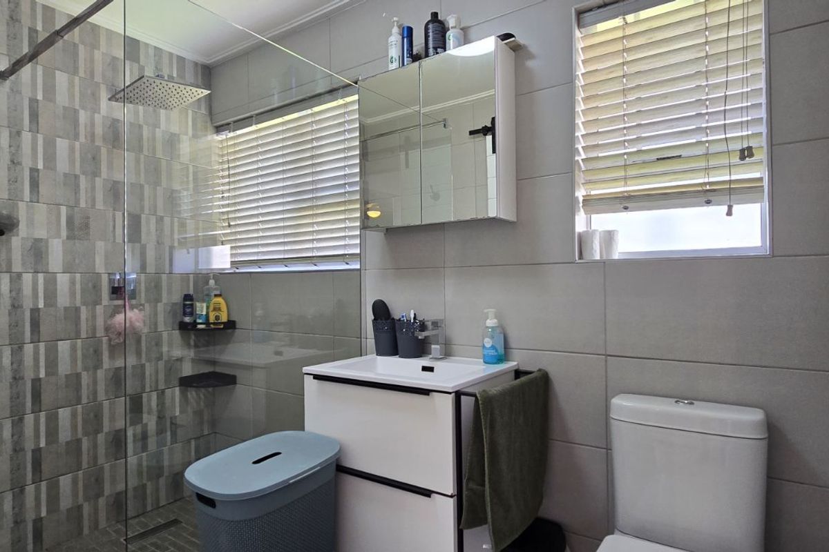 Modern bathroom featuring a glass-enclosed walk-in shower with rainfall showerhead, vanity cabinet with integrated basin, mirrored medicine cabinet, and neutral wall tiling.