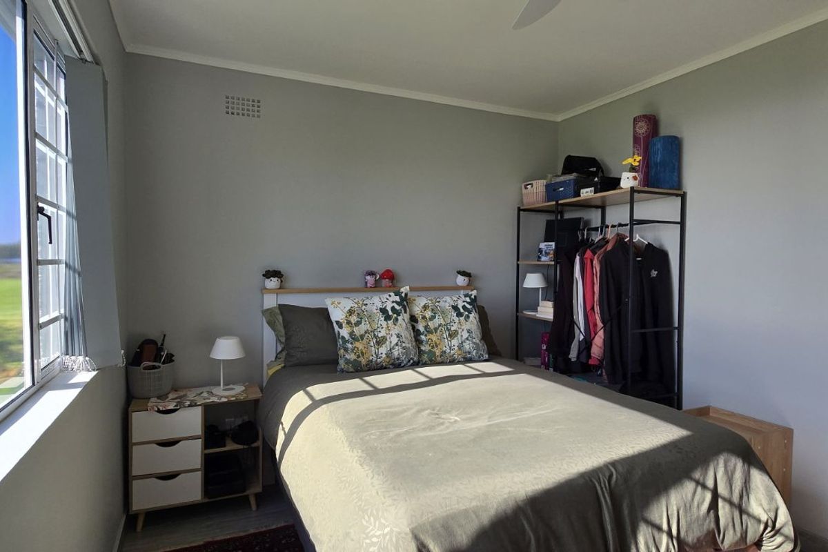 A bedroom featuring a large window with natural light, neutral wall finishes, and a ceiling fan.