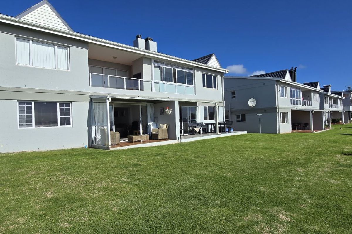 Rear view of the apartment complex featuring ground floor patios, upper level balconies, and a well-maintained communal lawn area.