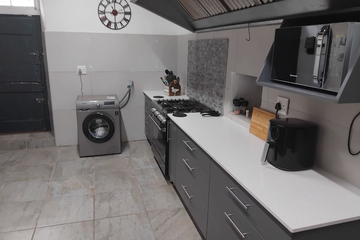 A functional kitchen featuring grey cabinetry, stone-look floor tiles, a gas hob, built-in oven, and integrated laundry plumbing.