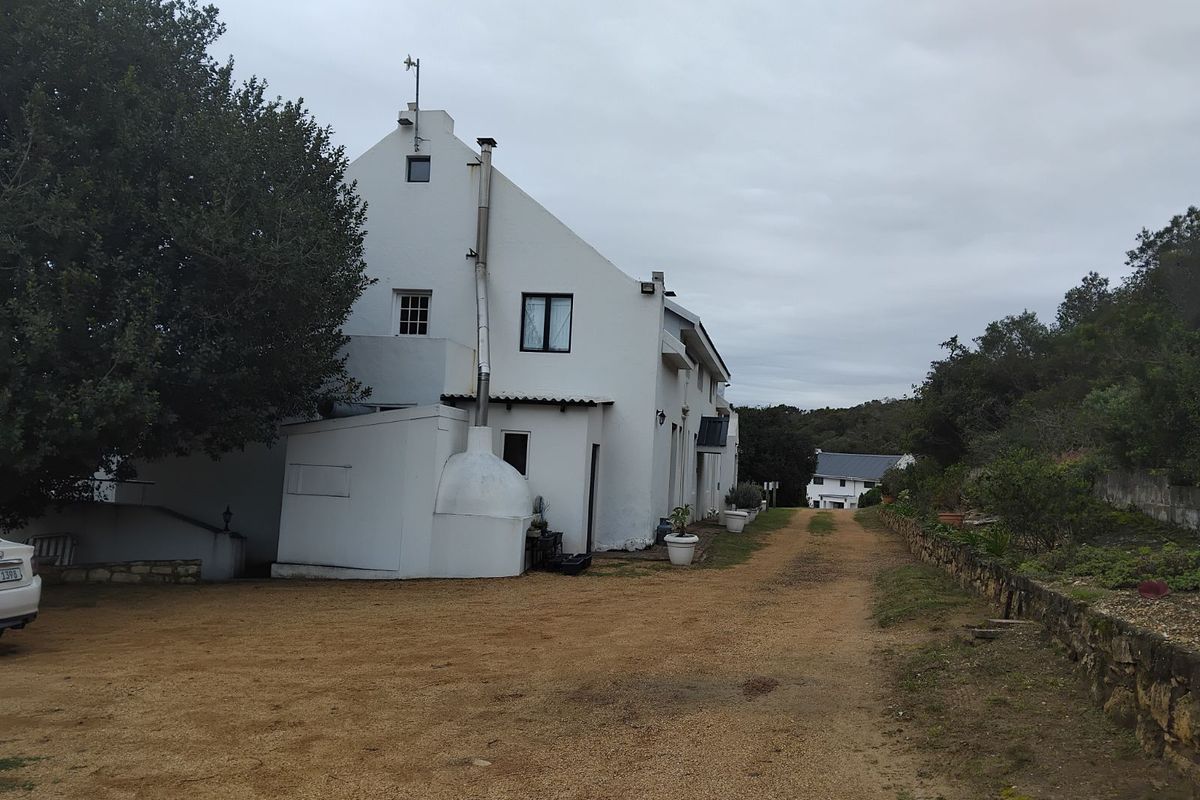 Side view of a white-painted house featuring a prominent external chimney, gravel driveway, and surrounding landscaped garden area.