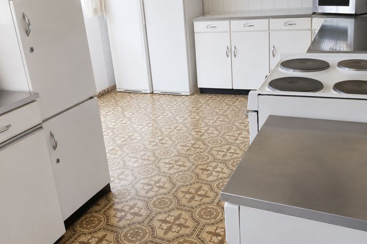 A dated kitchen featuring original patterned vinyl flooring, white cabinetry, and built-in appliances, offering significant potential for a modern renovation.