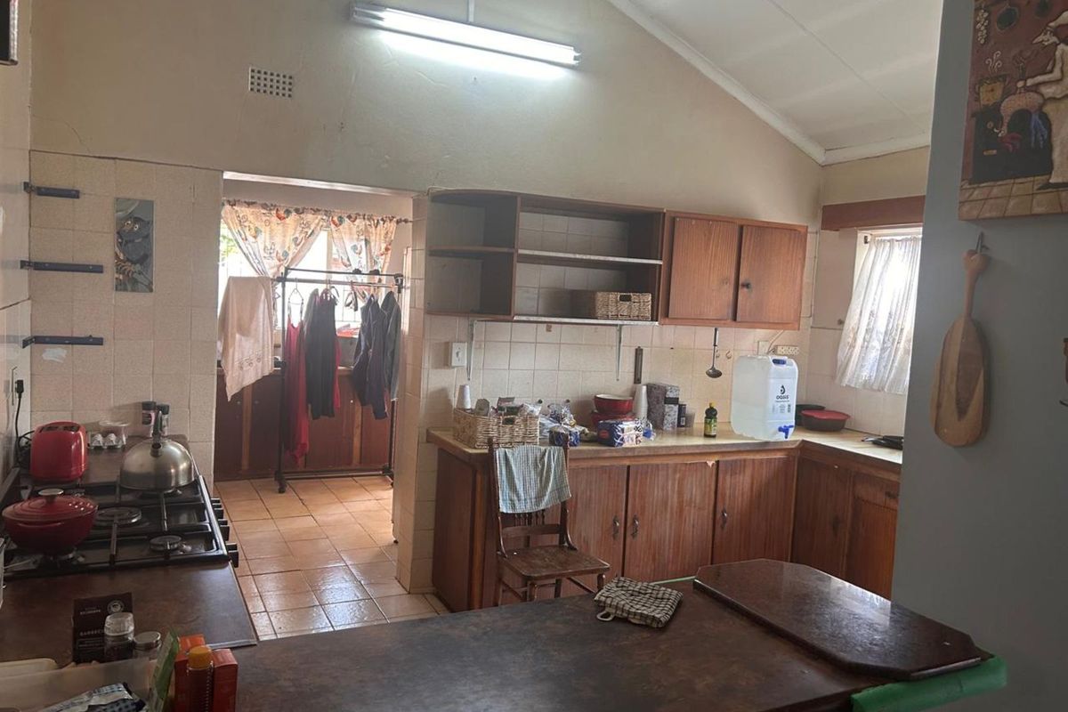 A dated kitchen featuring wooden cabinetry, tiled splashbacks, and a gas hob, with an adjacent scullery area visible through the doorway.
