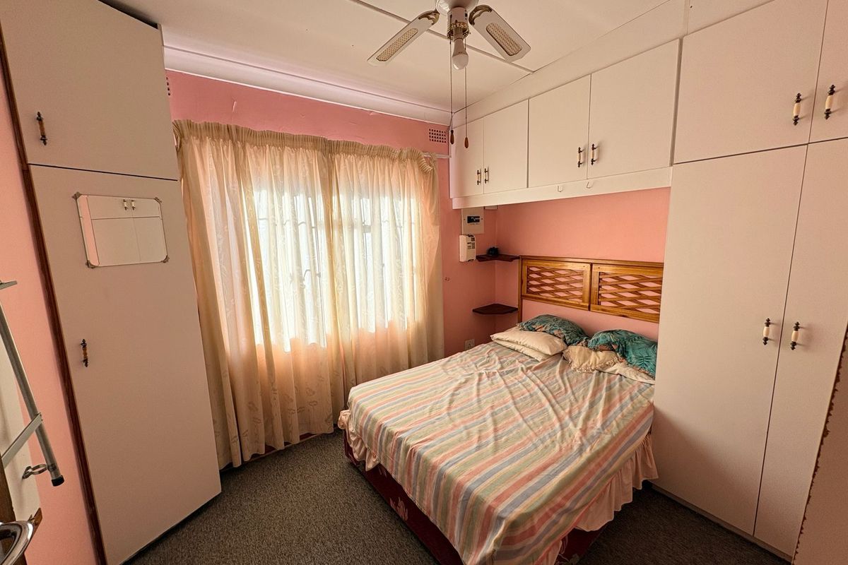 A bedroom featuring extensive built-in cabinetry, a ceiling fan, and carpeted flooring, offering functional storage space in a dated interior setting.