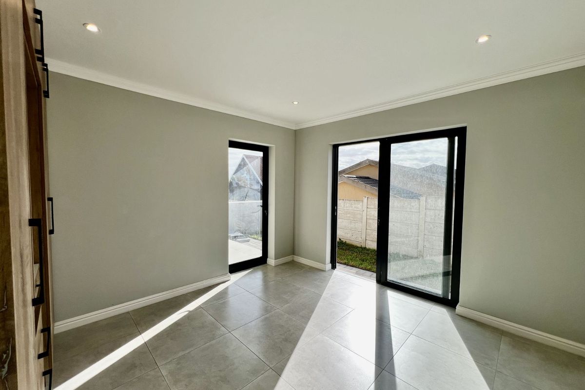 A bright, modern living area featuring large glass sliding doors, tiled flooring, and recessed ceiling lighting, offering direct access to the outdoor space.
