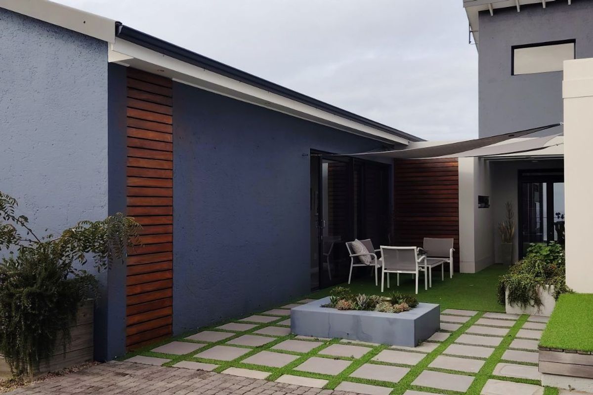 A modern rear patio area featuring paved sections, artificial turf, timber cladding accents, and a built-in planter box, providing a clean outdoor living space.