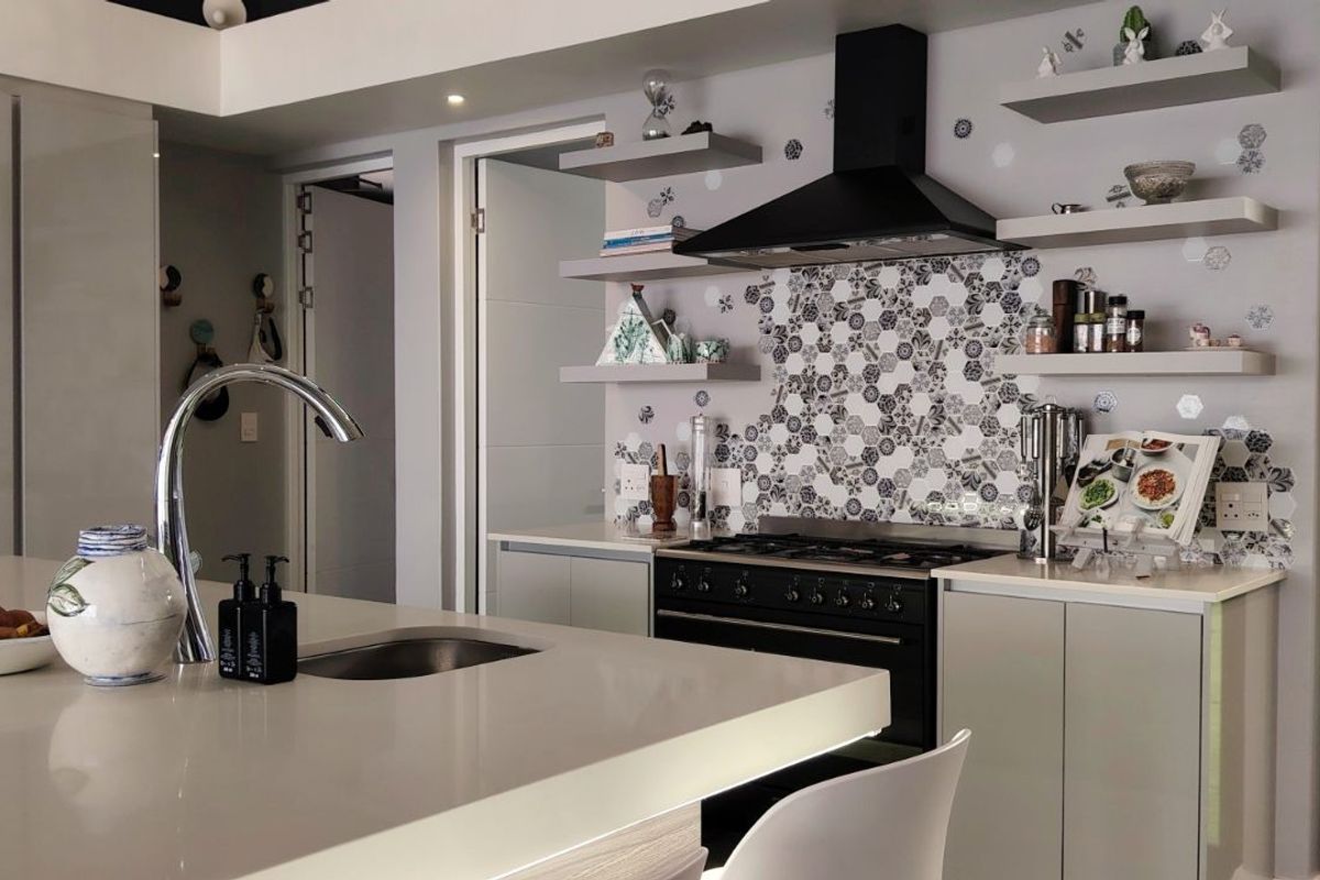 Modern kitchen featuring a central island with a sink, stone countertops, a gas range with a black extractor hood, and decorative hexagonal tile backsplash.