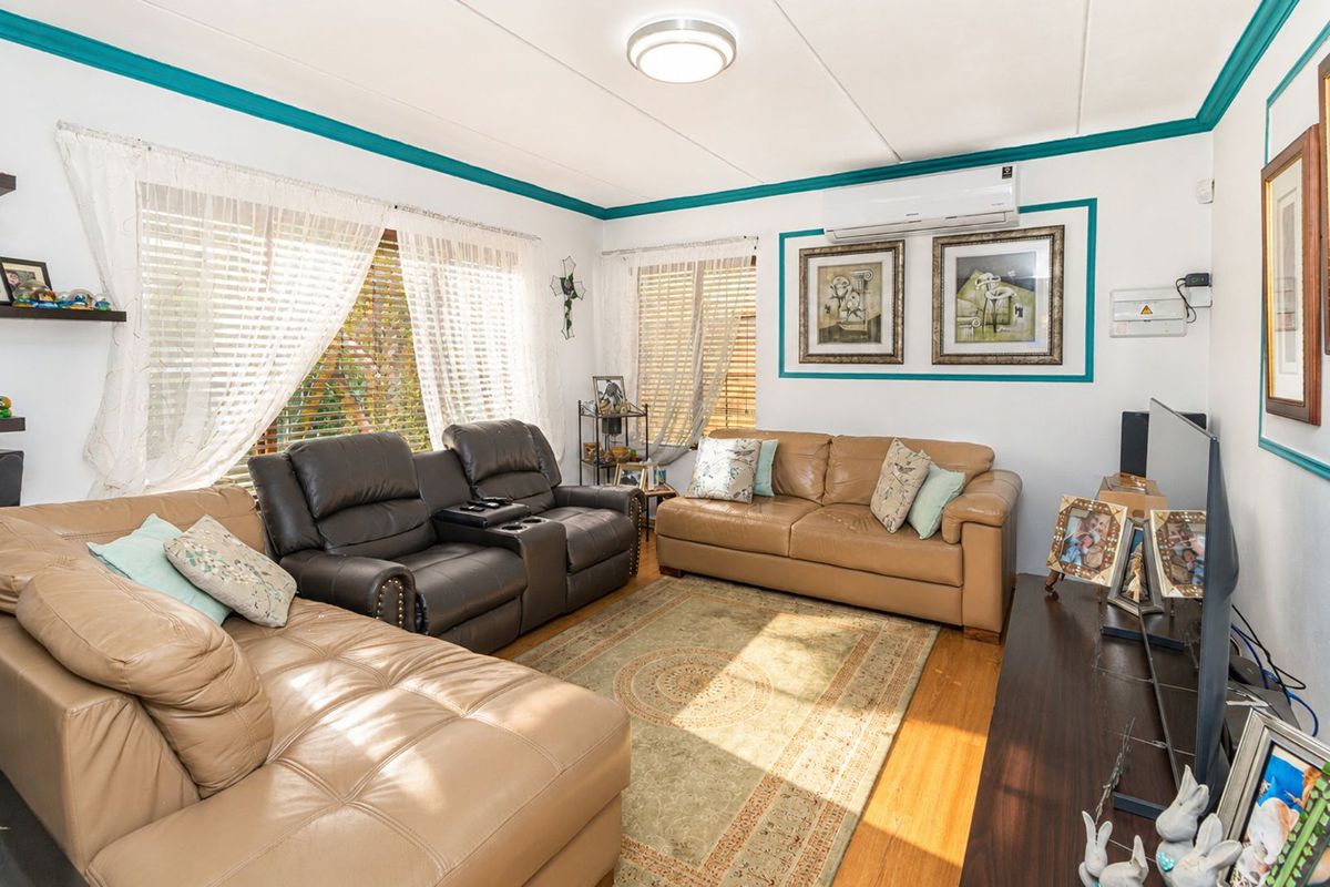 A comfortable living room featuring wood-look flooring, a wall-mounted air conditioning unit, and large windows allowing for natural light.