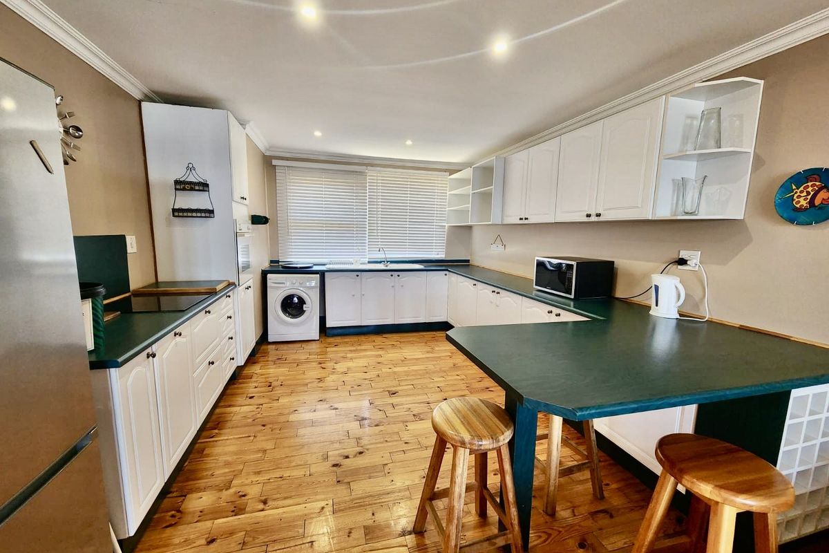 Spacious kitchen featuring white cabinetry, dark green countertops, integrated laundry appliance, and timber flooring with a breakfast bar area.