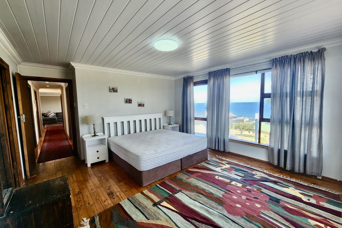 Spacious bedroom featuring timber flooring, tongue-and-groove ceiling, and large windows offering expansive ocean views.