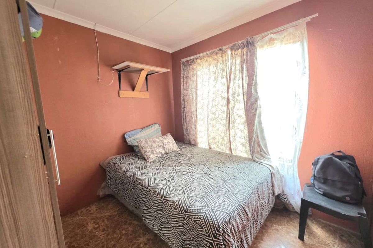 A compact bedroom featuring tiled flooring and terracotta-toned walls, providing a functional sleeping space with natural light from the window.