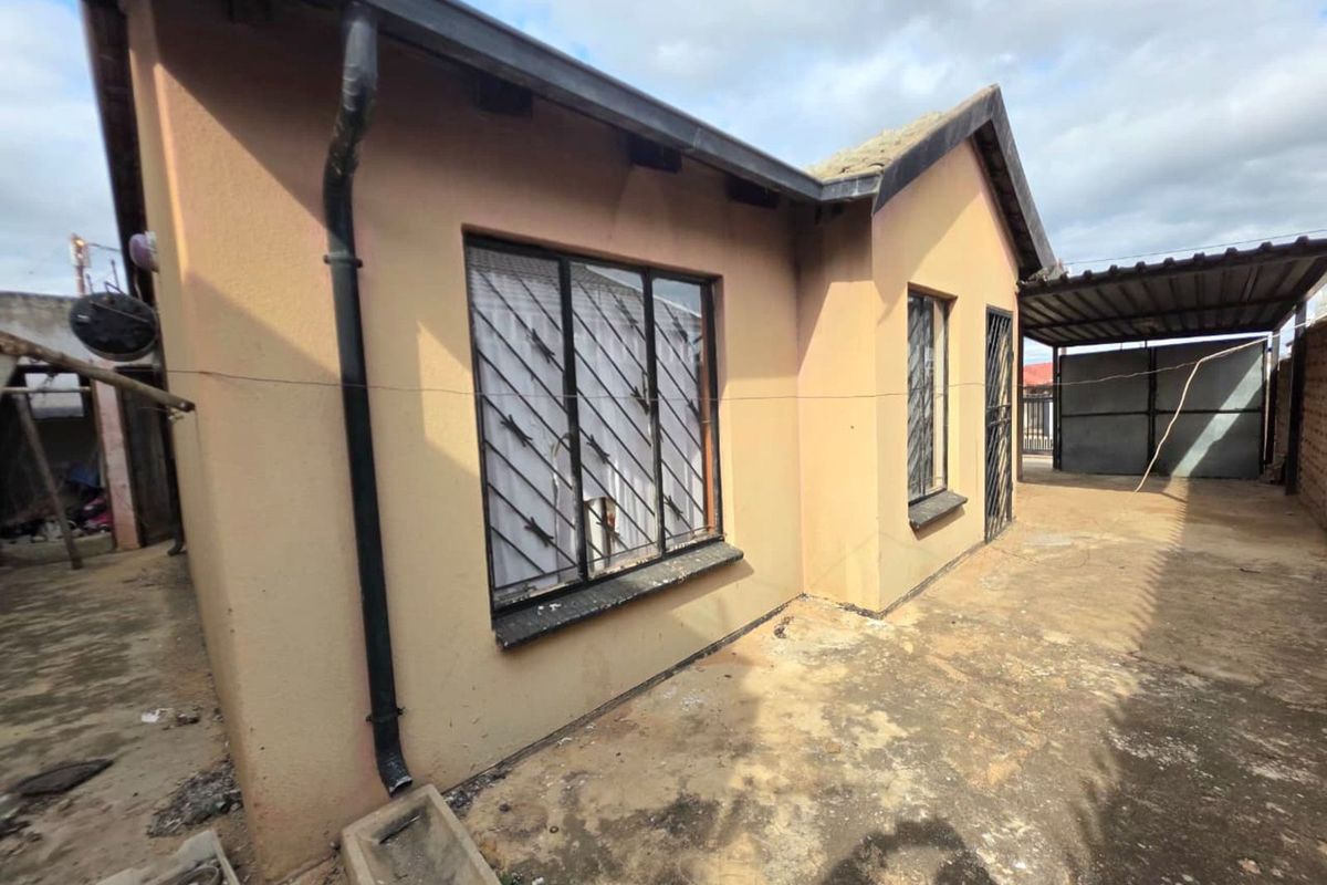Exterior view of the property showing the side facade, concrete paving, and metal security bars on the windows.