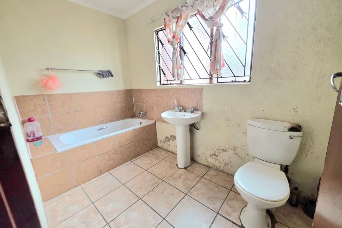 A dated bathroom featuring a tiled bathtub, pedestal basin, and toilet, requiring significant renovation and repair to address wall damage and finishes.