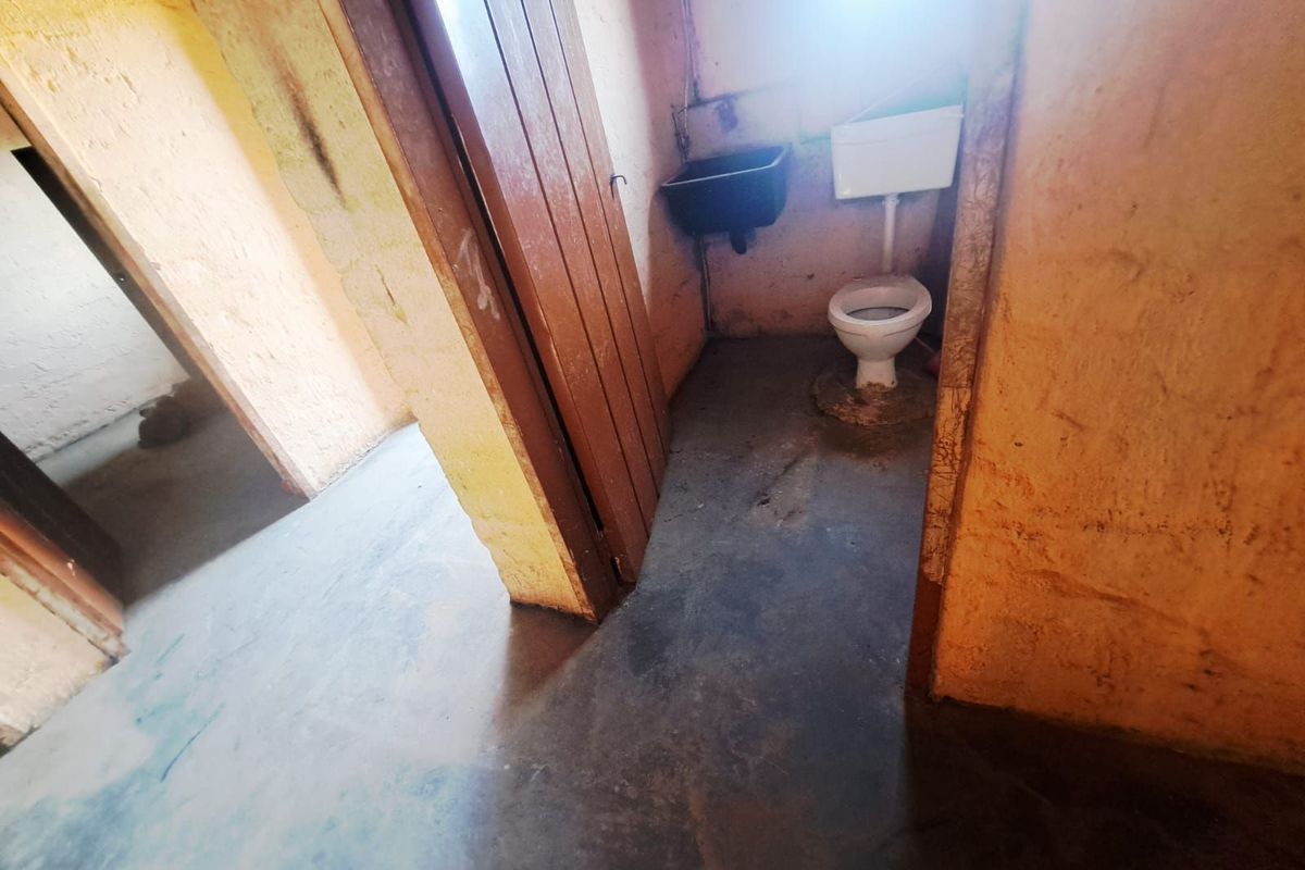 A basic, utilitarian bathroom featuring a standard toilet and wall-mounted basin, requiring significant renovation and cosmetic updates.
