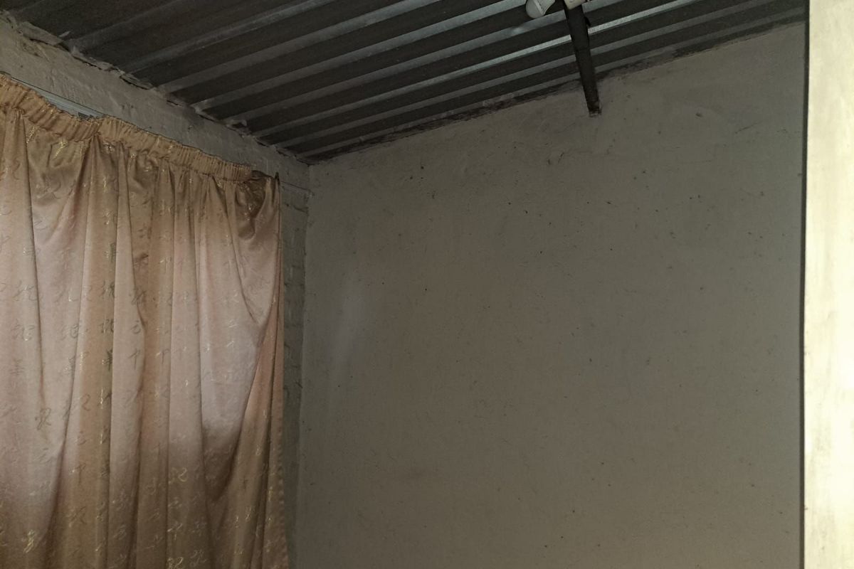 A basic interior room featuring unfinished wall surfaces and an exposed corrugated metal ceiling with a simple light fixture.