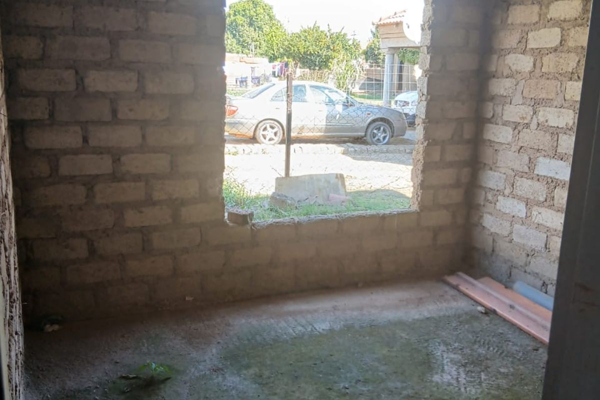 An unfinished room shell featuring exposed brick walls, an exposed roof structure, and a dirt floor, awaiting completion and interior finishes.