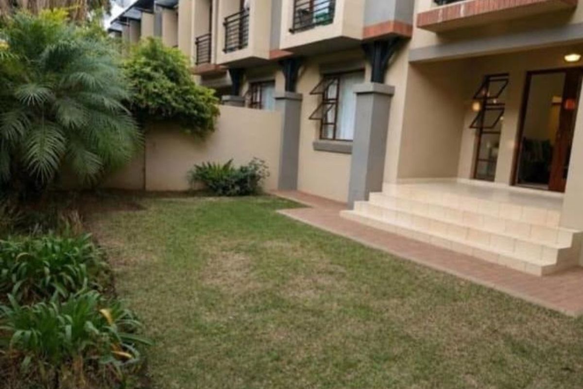 A private rear garden featuring a lawn area and a paved patio with steps leading to the building entrance.