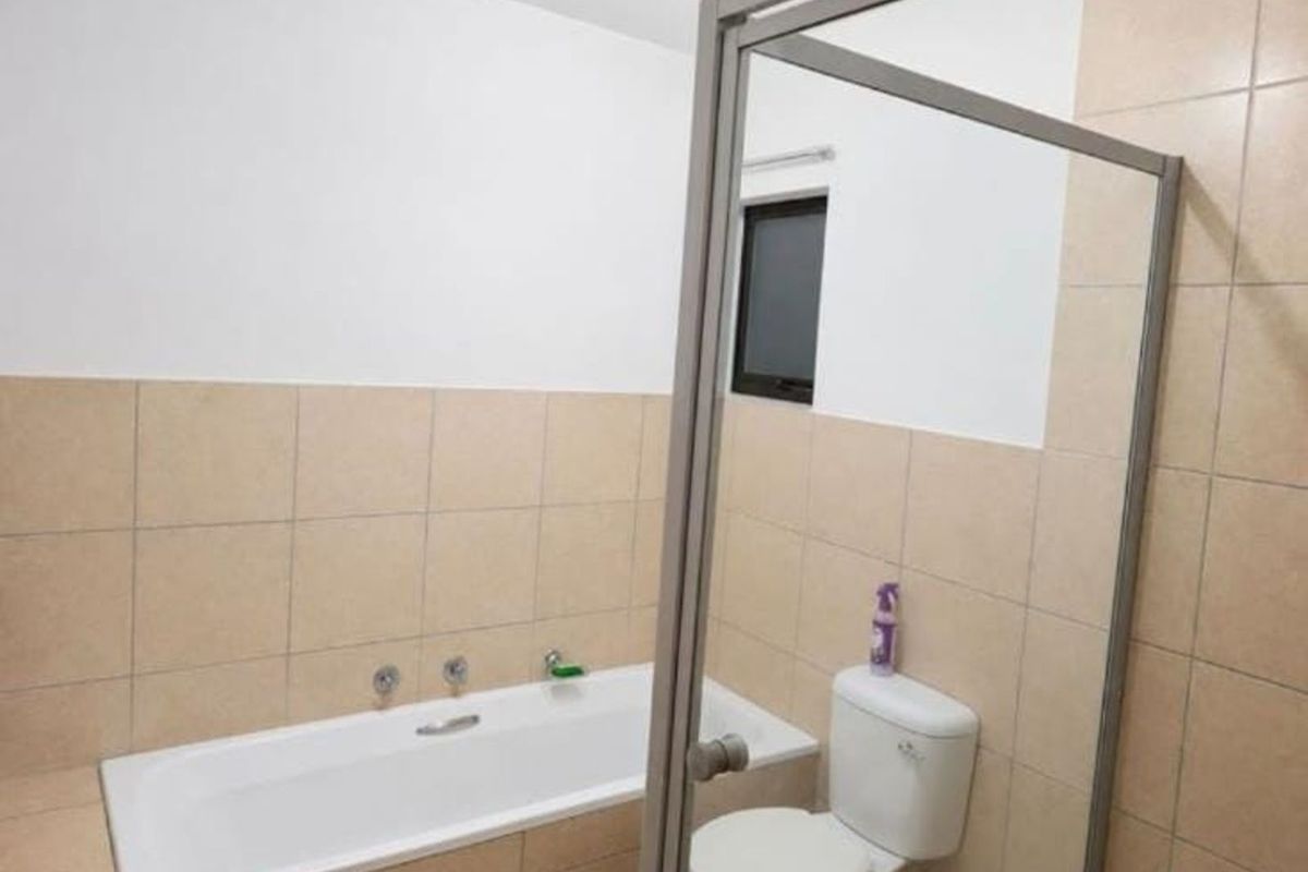 A functional bathroom featuring a built-in bathtub, a standard toilet, and neutral wall tiling.