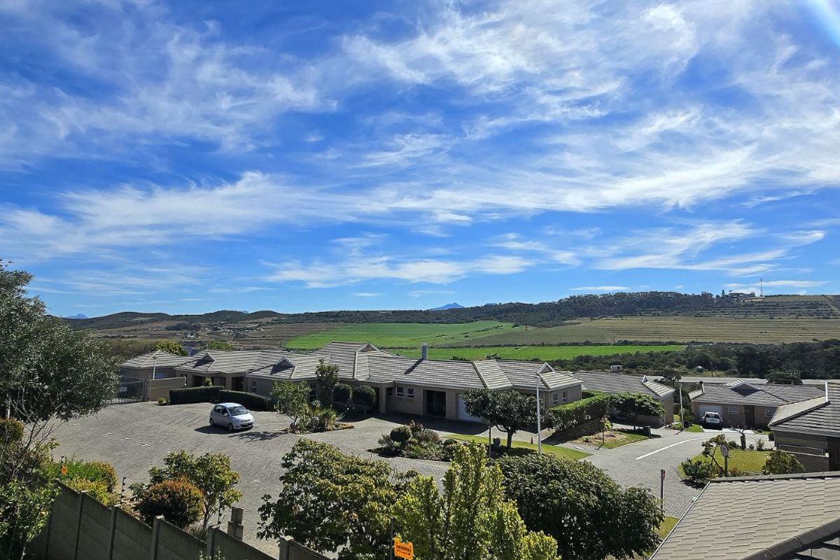 Elevated aerial view overlooking a residential estate with paved driveways, tiled roof structures, and expansive green landscape vistas in the background.