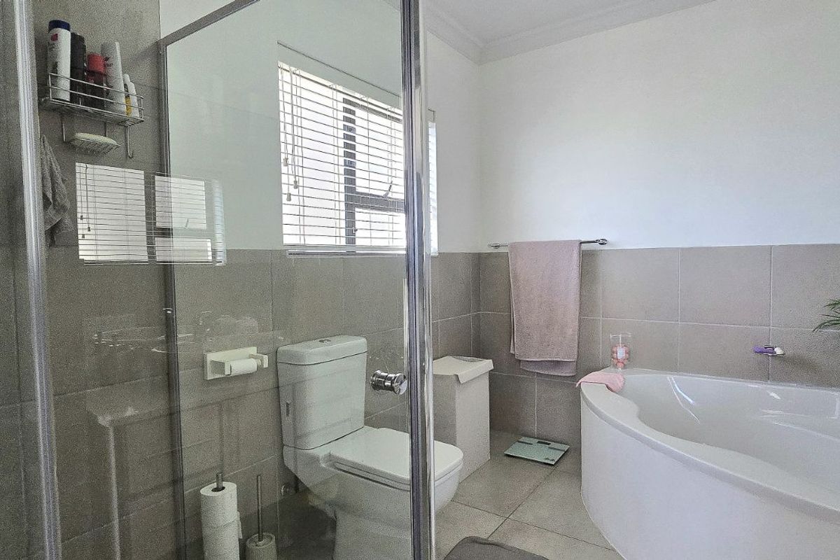 A modern bathroom featuring a glass-enclosed shower, a corner bathtub, a toilet, and neutral wall and floor tiling.