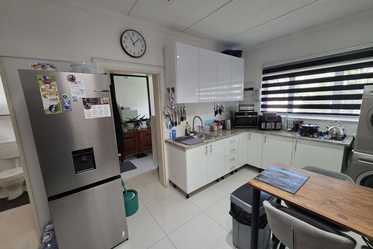 A functional kitchen featuring white cabinetry, stone-look countertops, a stainless steel sink, and a built-in gas hob, with tiled flooring throughout.