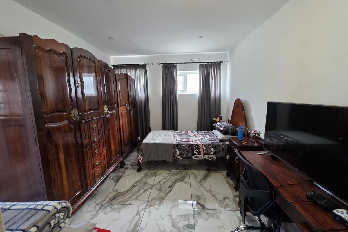 A bedroom featuring large built-in wooden wardrobes, marble-look tiled flooring, and a window with curtain tracks.