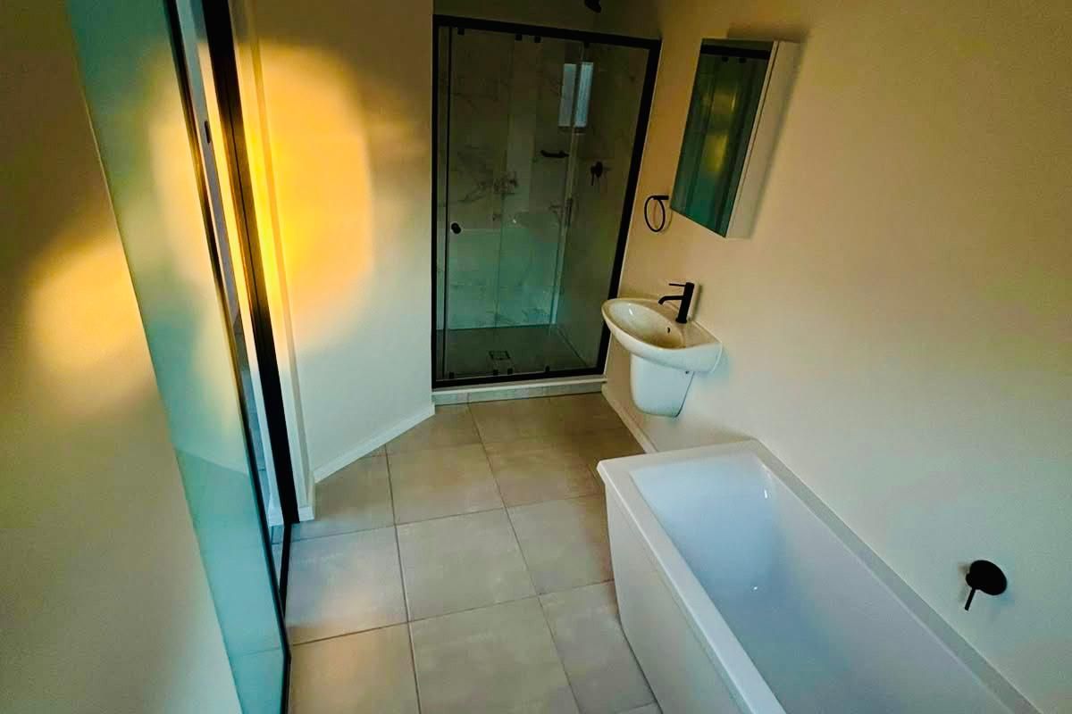 A modern bathroom featuring a built-in bathtub, a separate glass-enclosed shower, a wall-mounted basin, and a toilet with neutral floor tiling.