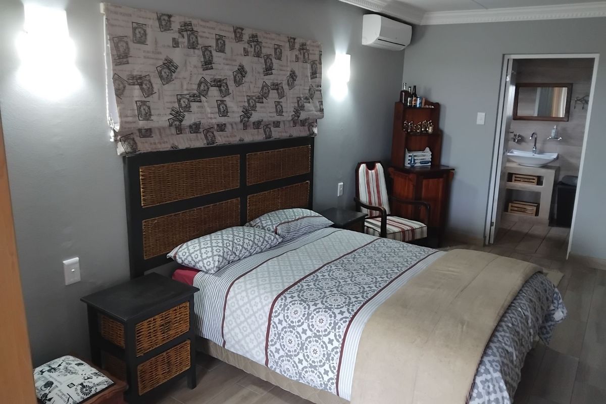A well-maintained bedroom featuring tiled flooring, wall-mounted air conditioning, and an en-suite bathroom with a modern vanity basin.