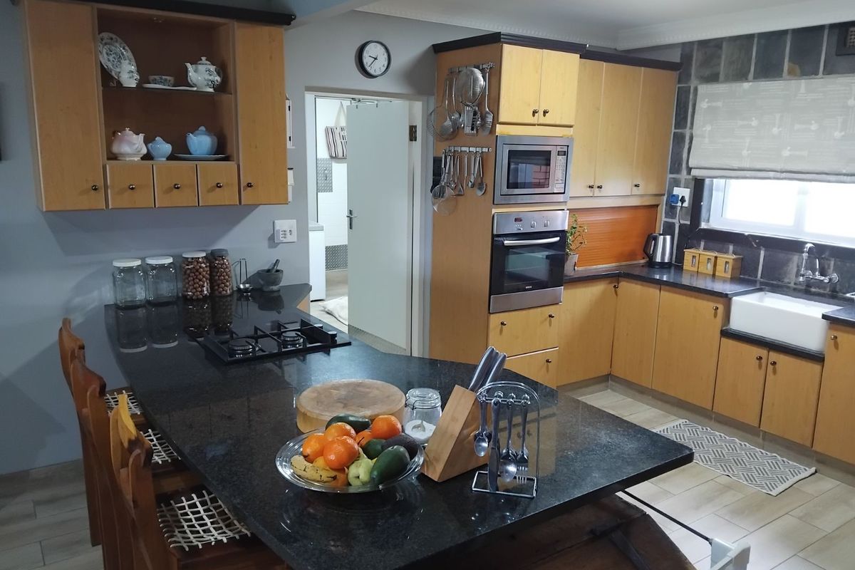 A functional kitchen featuring wooden cabinetry, dark granite countertops, a built-in oven, microwave, and a farmhouse-style sink with a breakfast bar island.