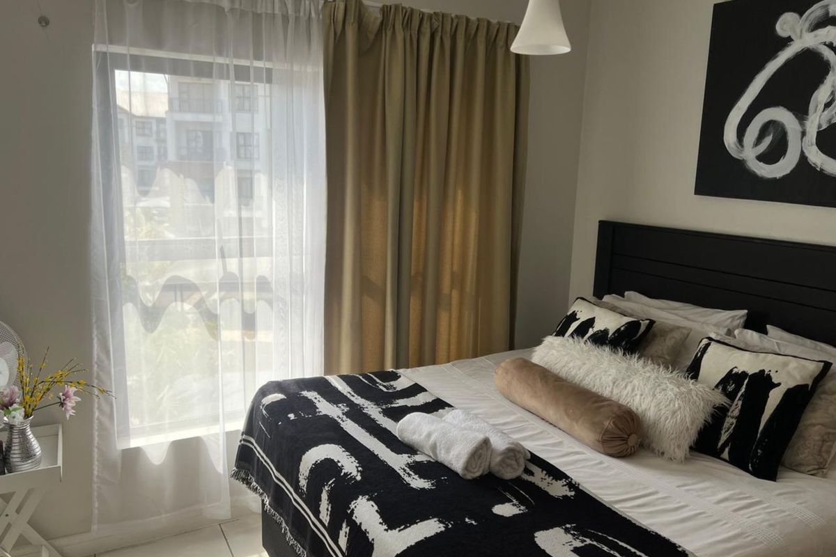 A well-lit bedroom featuring neutral wall tones, tiled flooring, and a large window with curtain treatments.